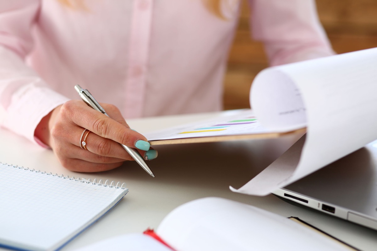 Female hands hold silver pen and pad with financial statistics at workplace closeup; NLRB certification concept