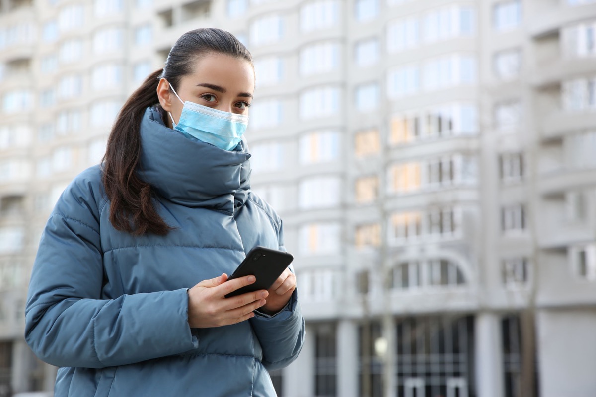 Woman with disposable mask and smartphone outdoors; pandemic safety