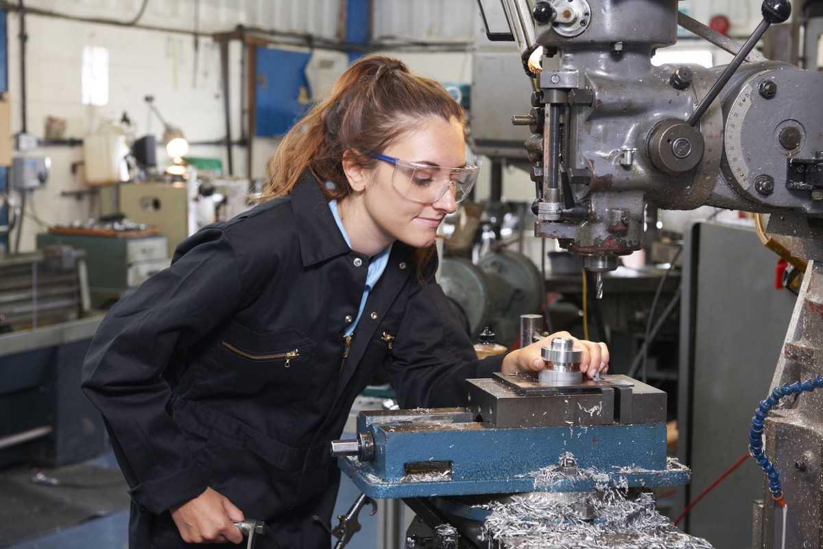 Female Apprentice Engineer Working On Drill In Factory; IAM essential workers concept