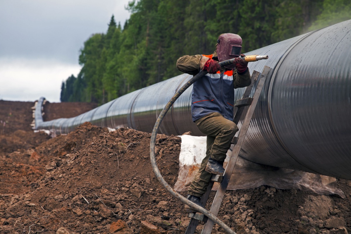Worker using a sandblaster cleans tubing pipe before insulation; IUOE union profile concept
