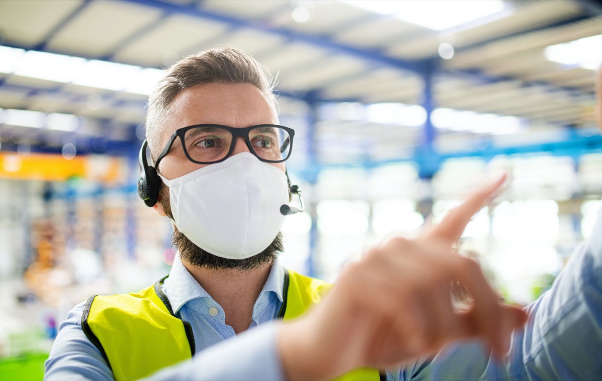 Side view of technician with protective mask working in industrial factory; support front-line workers concept.