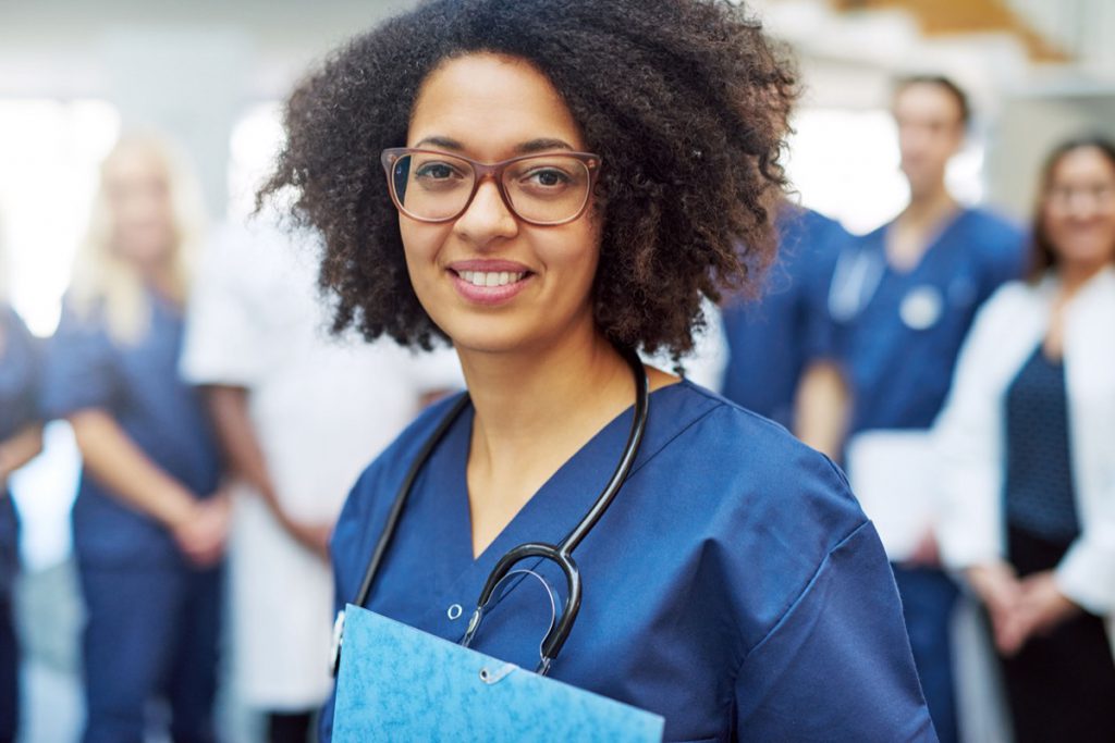Young black female doctor looking at camera in a hospital standing in front of medical team