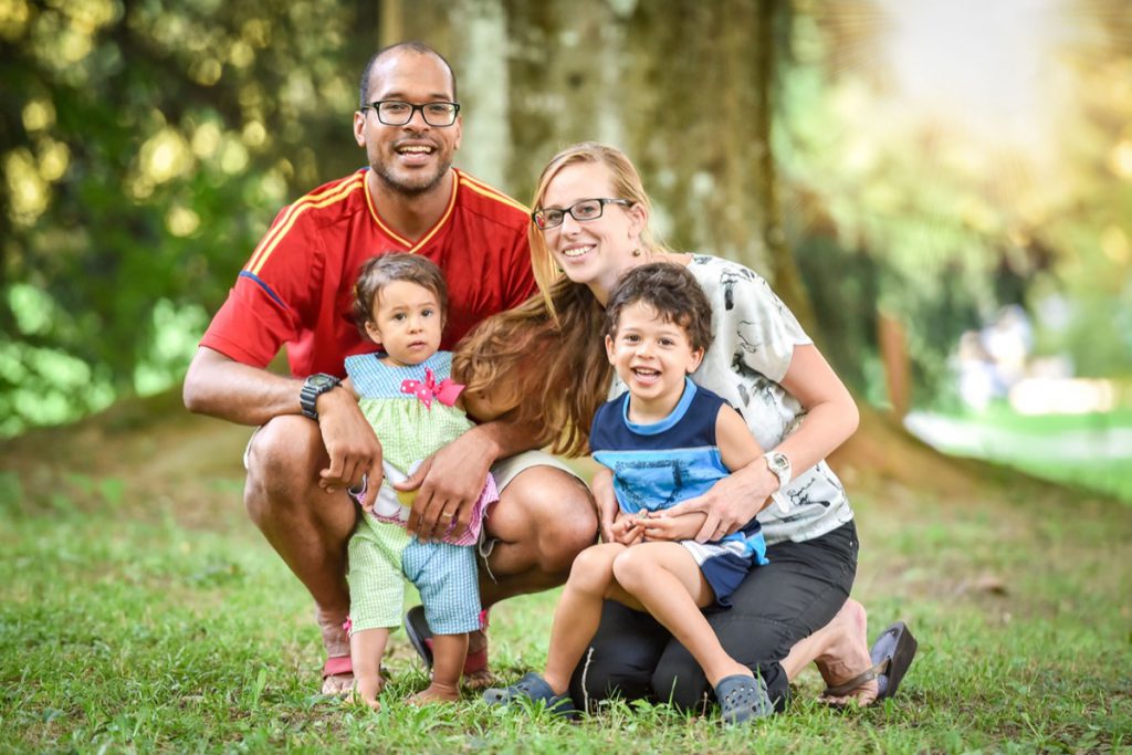 Happy interracial family is enjoying a day in the park. Little mulatto baby girl and boy. Successful adoption. Diverse family in nature with sun in the back.