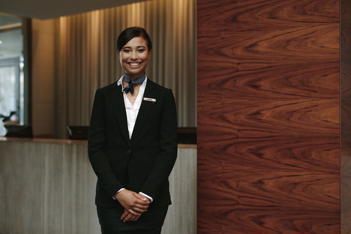 Portrait of happy female hotel receptionist standing at workplace; travel industry workers concept