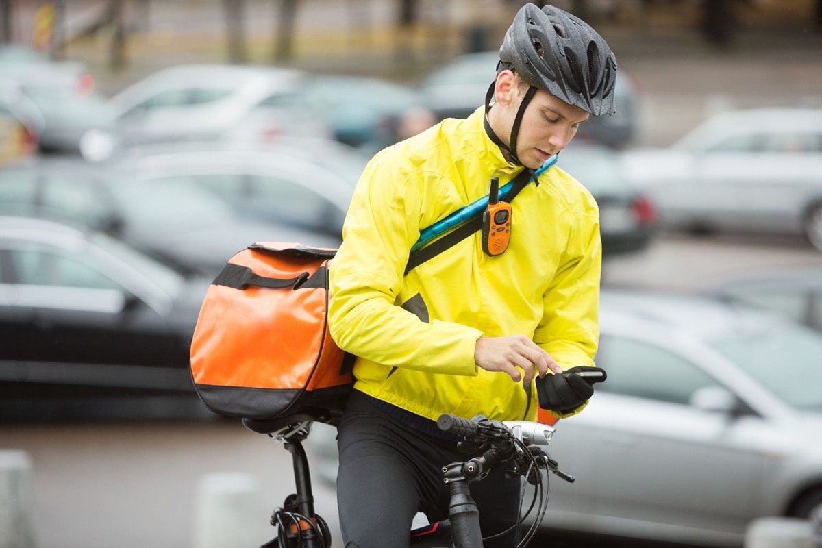 male cyclist with courier bag using mobile phone on street; gig and tech workers need unions concept