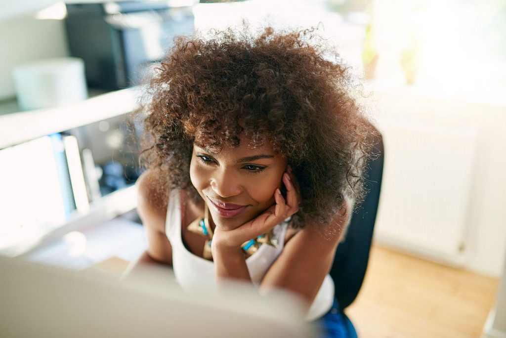 Black smiling girl using small business computer on blurred inside background.
