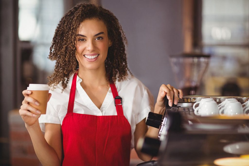 Portrait of a waitress holding a take-away mug at the coffee shop